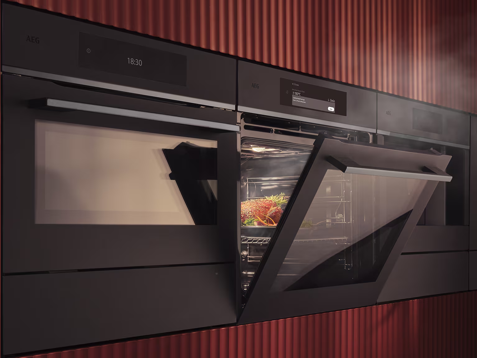 AEG built-in ovens with doors open in a ribbed deep red kitchen run